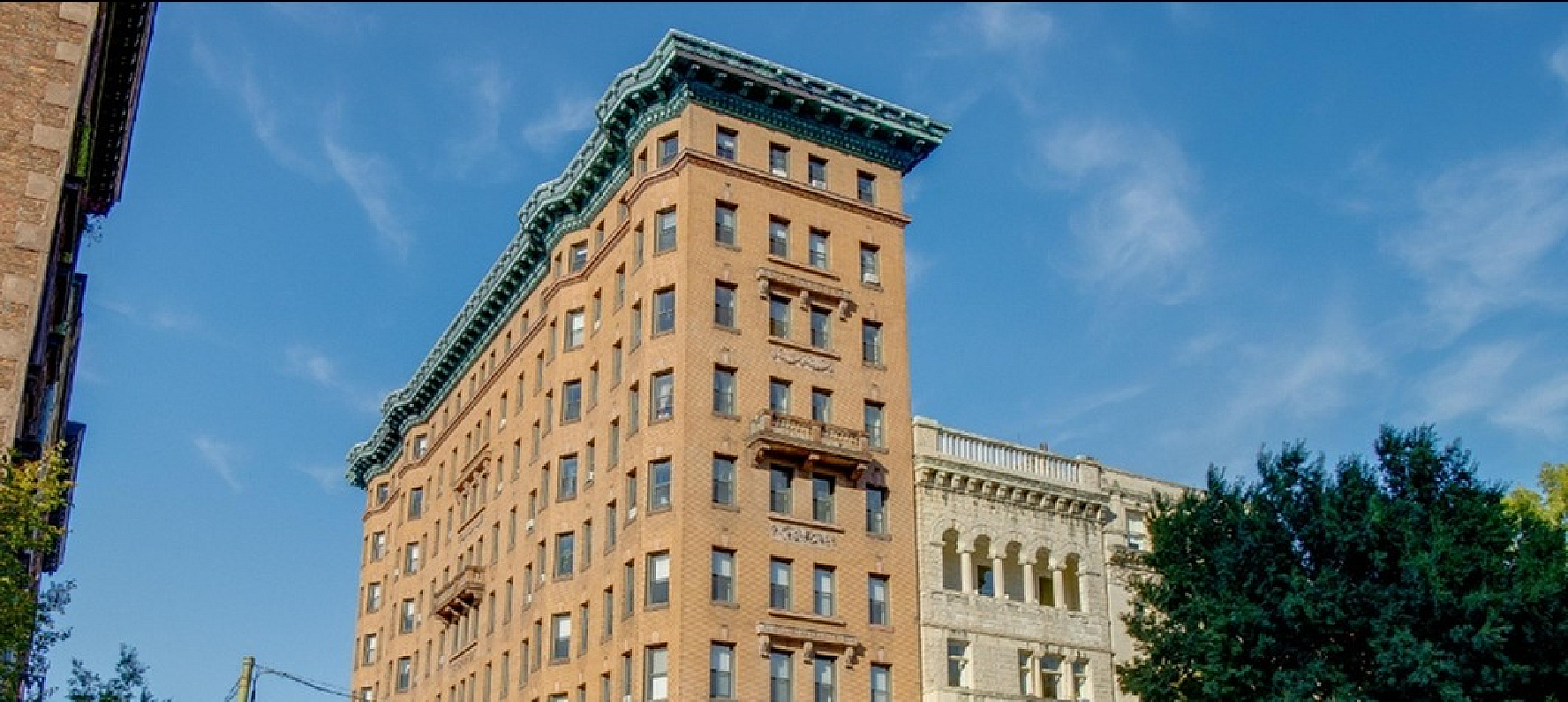 Charming historic apartment building set amidst a vibrant cityscape, showcasing classic architecture and lush greenery on a sunny day.