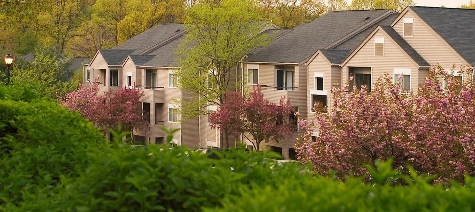 Charming apartment complex surrounded by lush greenery and vibrant spring blossoms, featuring modern architecture and a serene atmosphere.