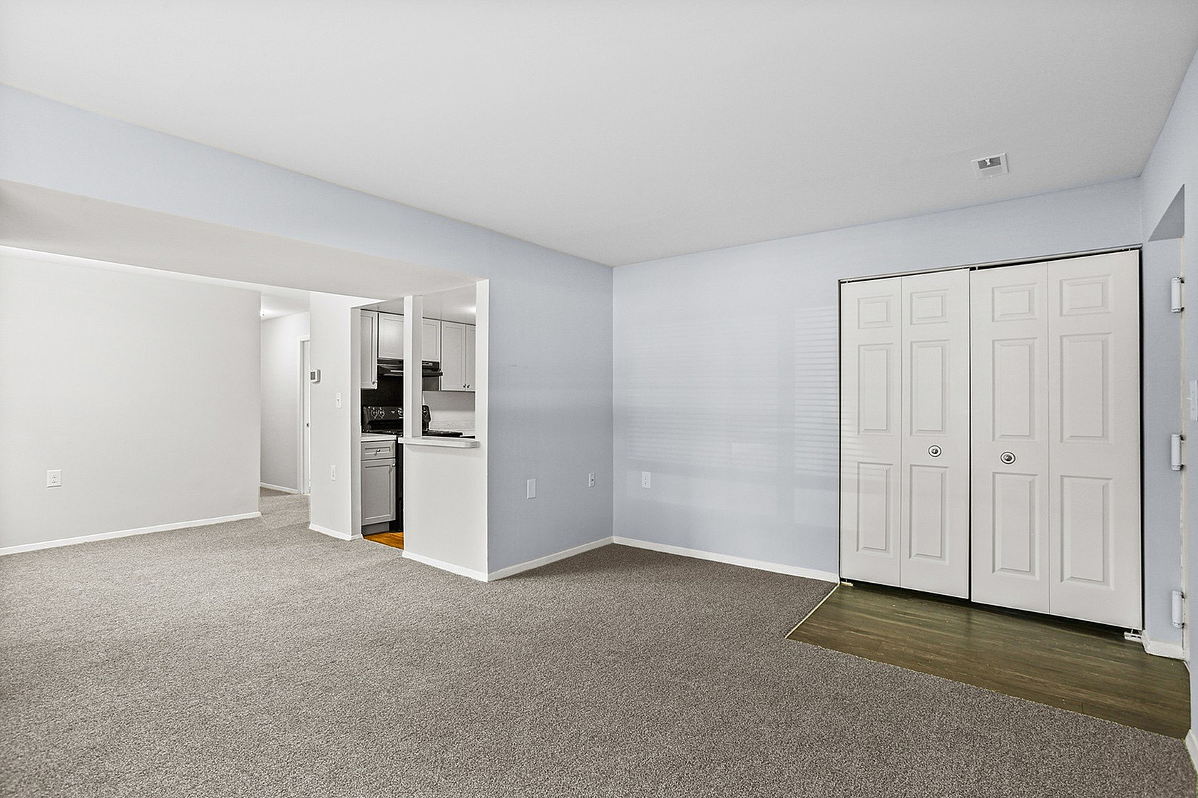 Bright and inviting open living area with neutral tones, plush carpeting, and a modern kitchen alcove. Features ample natural light and sleek closet space.