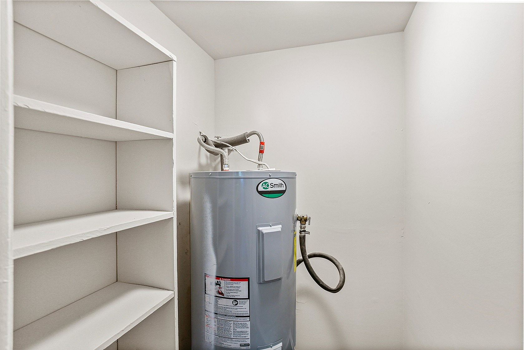 Efficient utility room featuring a brand-new water heater and convenient built-in shelving for optimal storage.