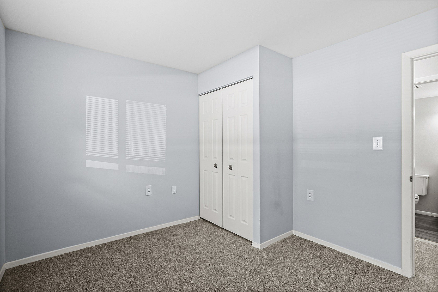 Bright and inviting bedroom with soft gray walls, plush carpet, and a spacious closet, perfect for cozy living.