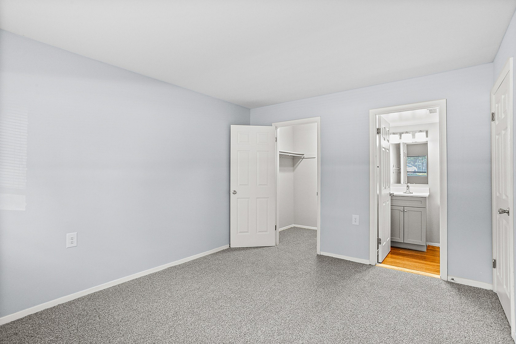 Bright and airy bedroom featuring plush carpeting, a walk-in closet, and an en-suite bathroom with modern fixtures.