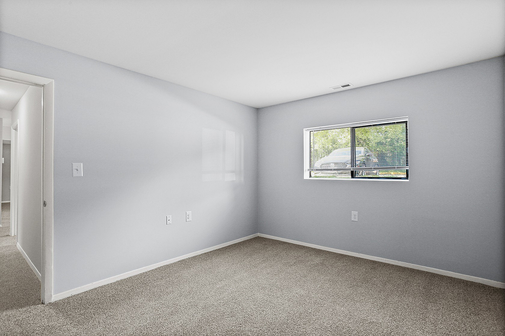 Bright, spacious room with soft carpet flooring and a large window inviting natural light, creating a warm, inviting atmosphere.