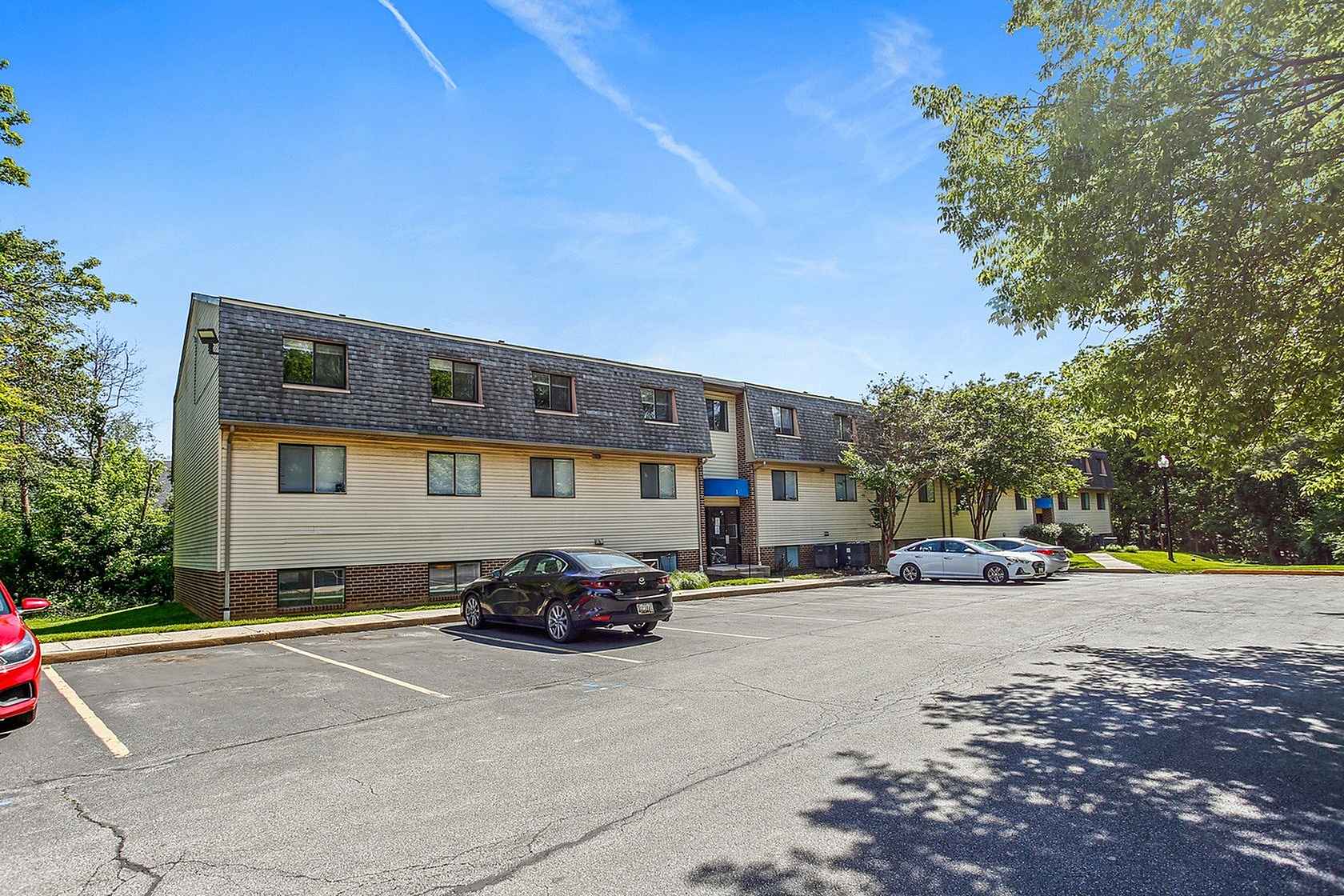 Charming apartment complex with well-maintained exterior, surrounded by lush greenery and clear blue skies.