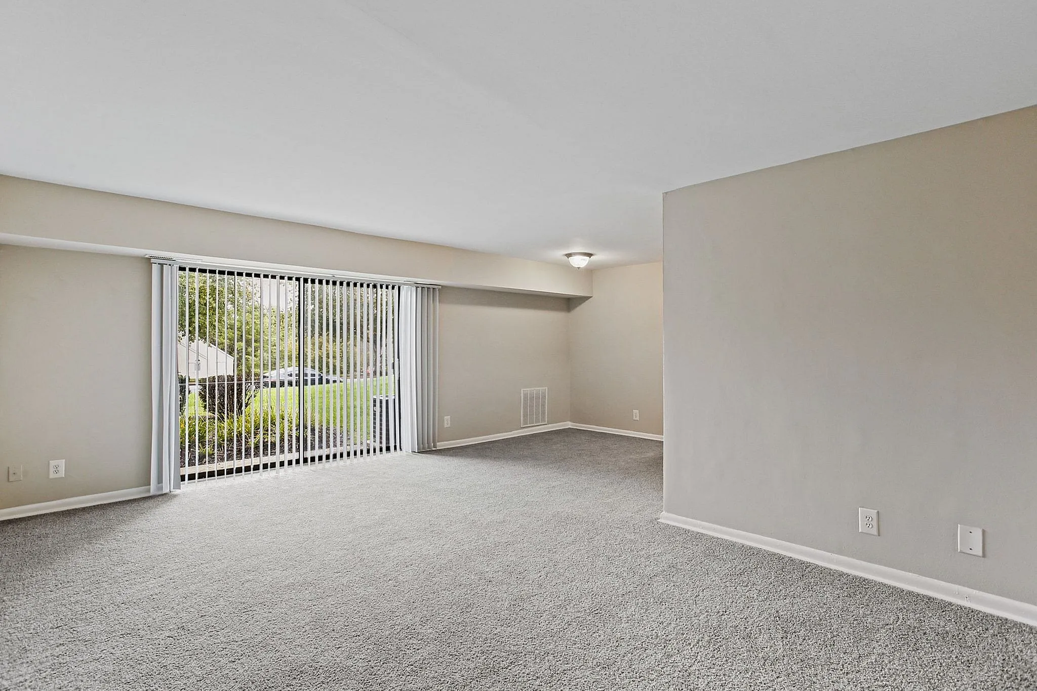 Bright and spacious living room with lush garden views through large sliding glass doors, featuring plush carpet and neutral walls.