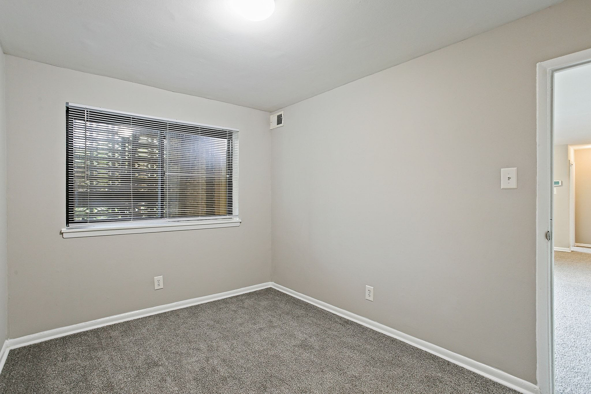 Cozy room with modern carpet flooring, bright window with blinds, and soft neutral wall tones.
