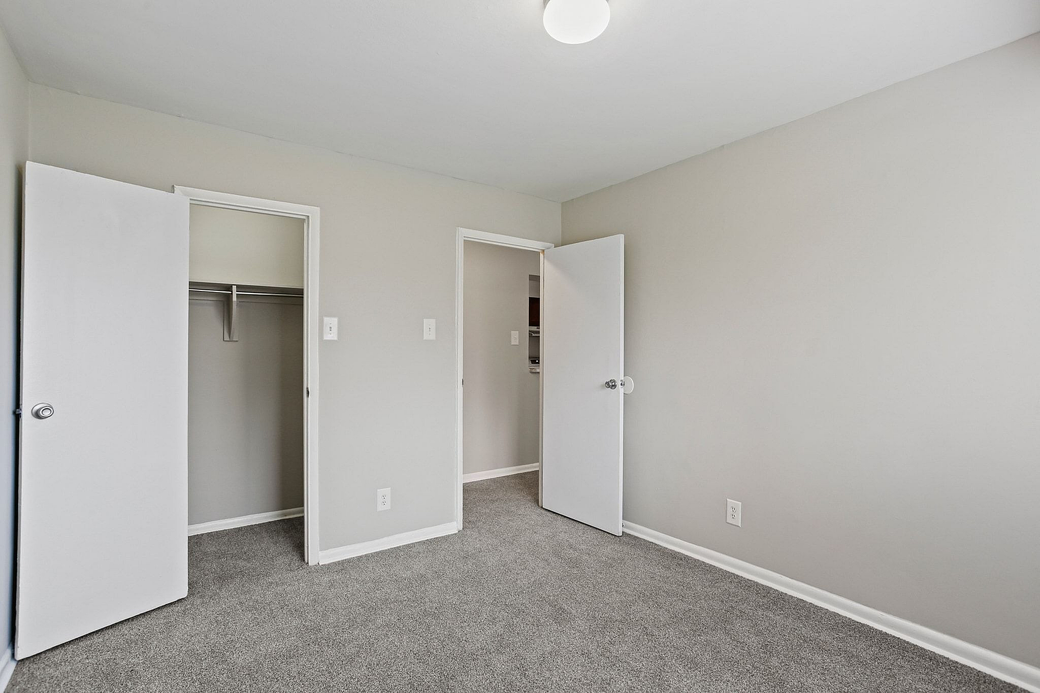 Bright and spacious bedroom with fresh grey carpeting, featuring a large closet and sleek white doors, perfect for modern living.