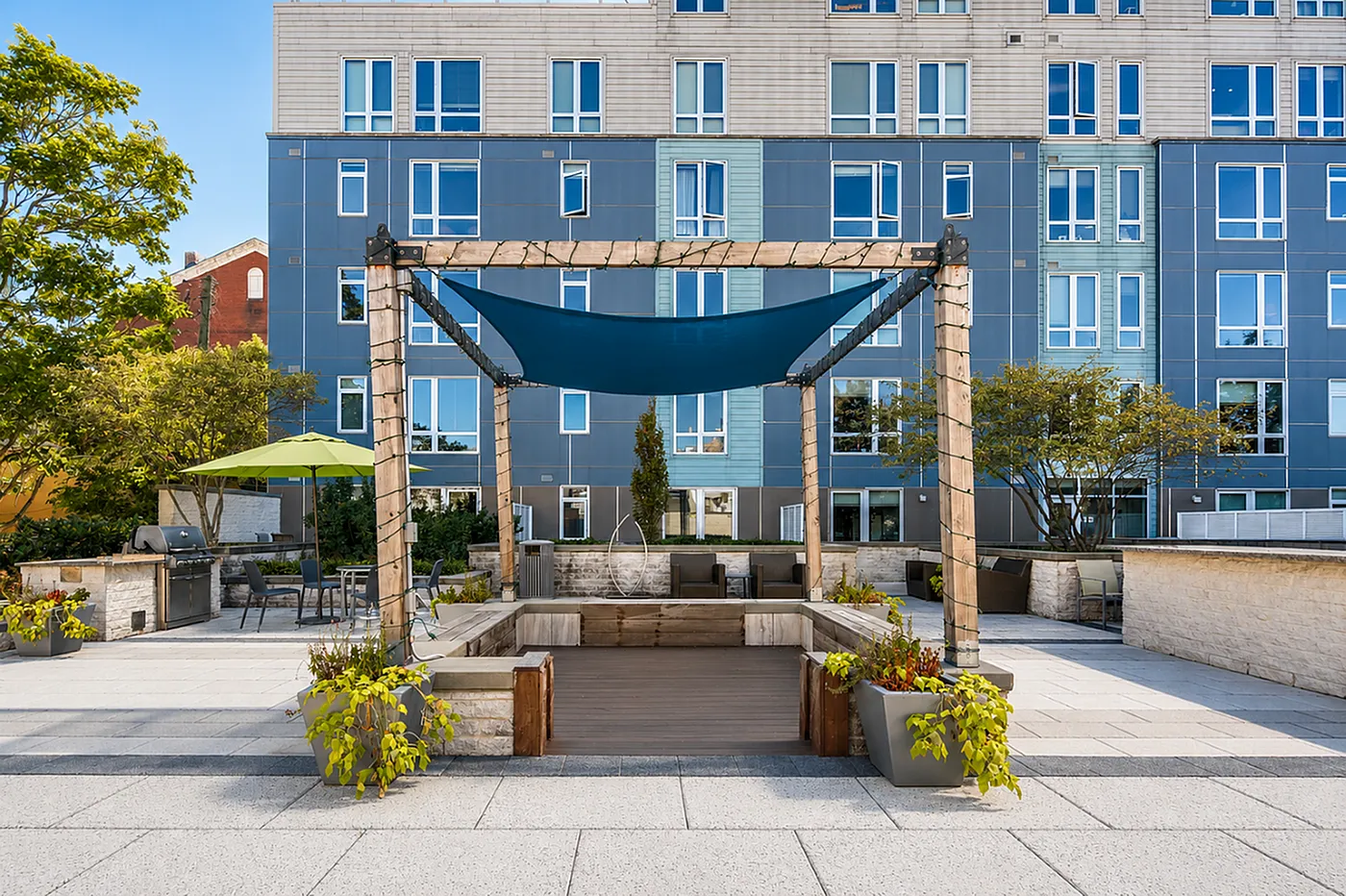 Modern apartment exterior with vibrant blue panels, featuring a stylish outdoor seating area under a wooden pergola with lush greenery.