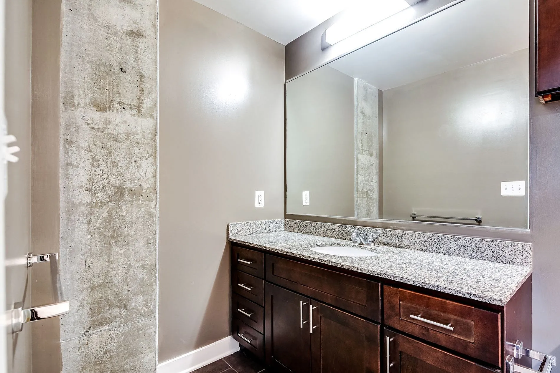 Elegant bathroom featuring a large mirror, sleek granite countertop, and modern dark wood cabinetry.