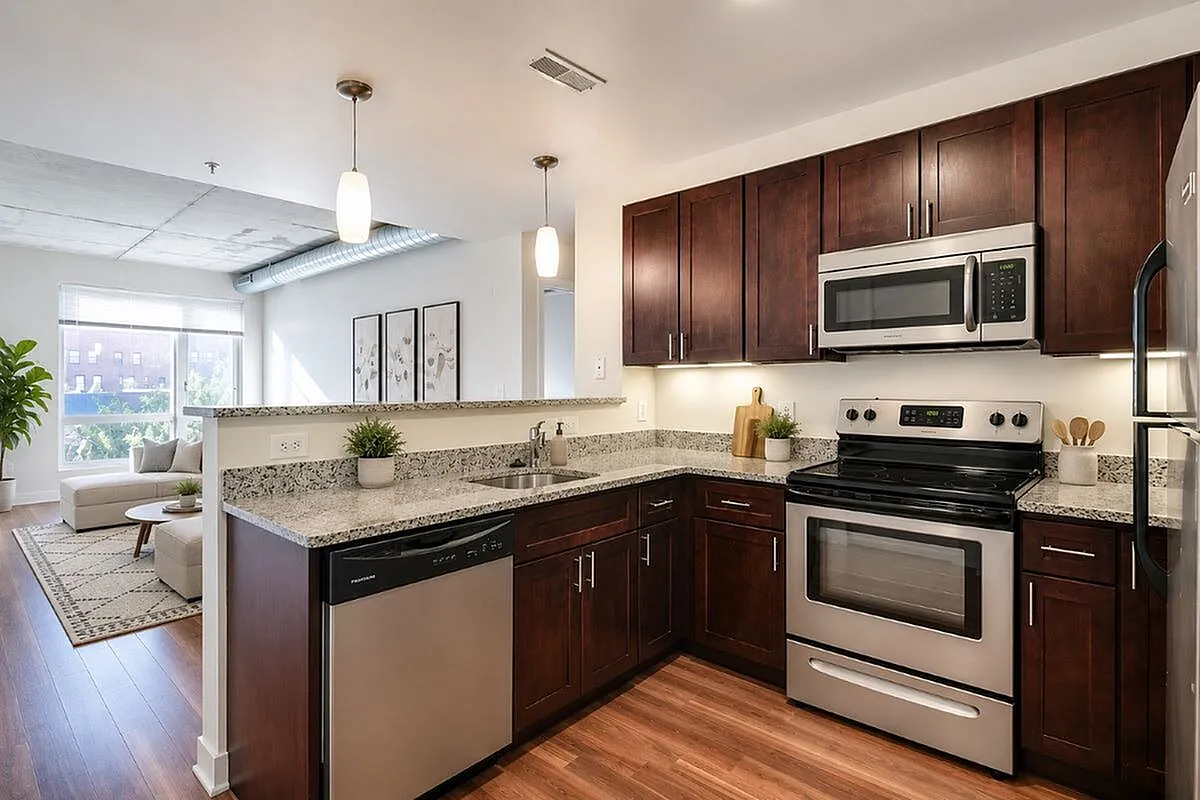 Modern kitchen with stainless steel appliances and granite countertops opening to a bright living room with large window views.