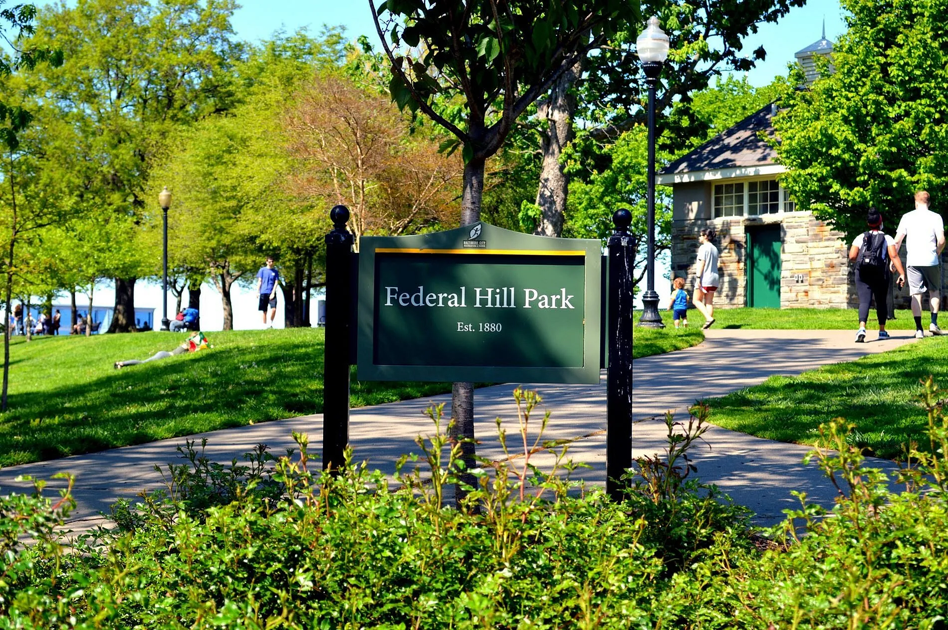 Vibrant Federal Hill Park on a sunny day, featuring lush greenery, a historic sign, and people enjoying the outdoors.