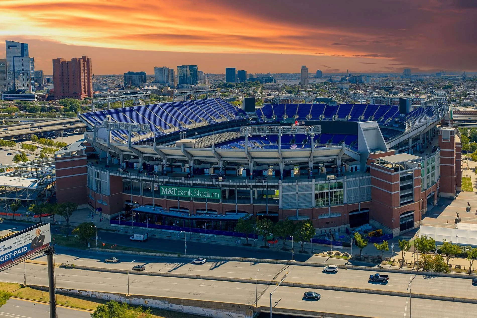 Aerial view of a bustling stadium surrounded by cityscape, illuminated by a vibrant sunset, offering a lively atmosphere.