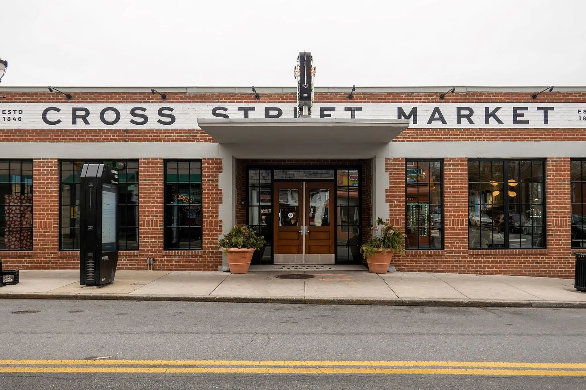 Charming entrance of Cross Street Market featuring classic brick exterior, large windows, and welcoming double doors.