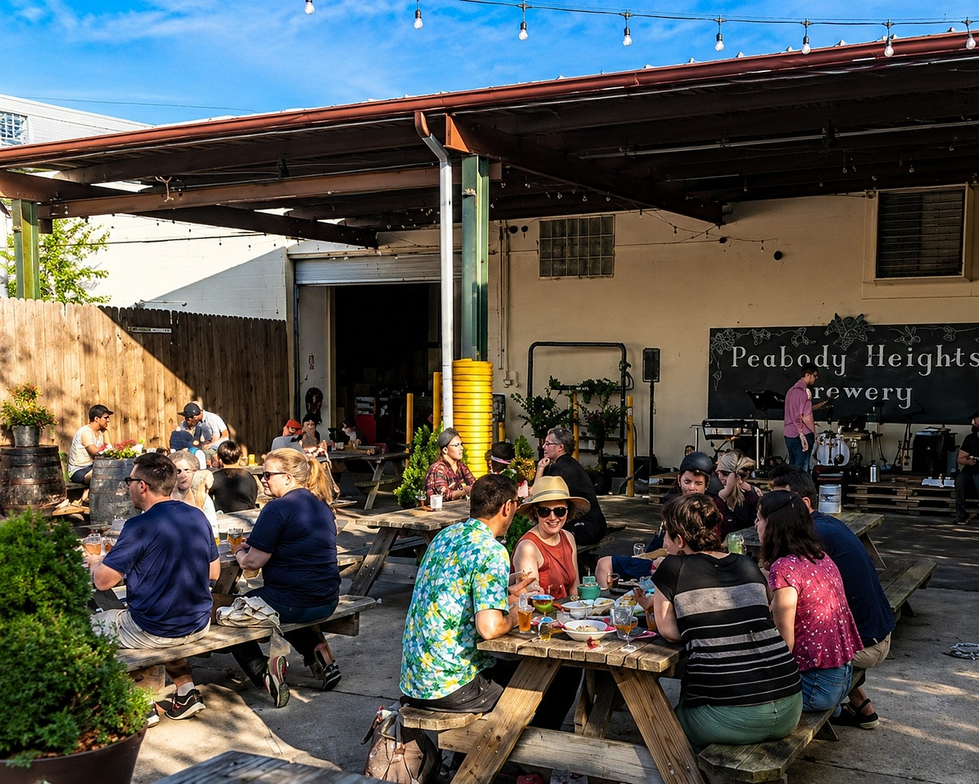 Vibrant outdoor seating area at Peabody Heights Brewery with people enjoying drinks and live music under string lights.