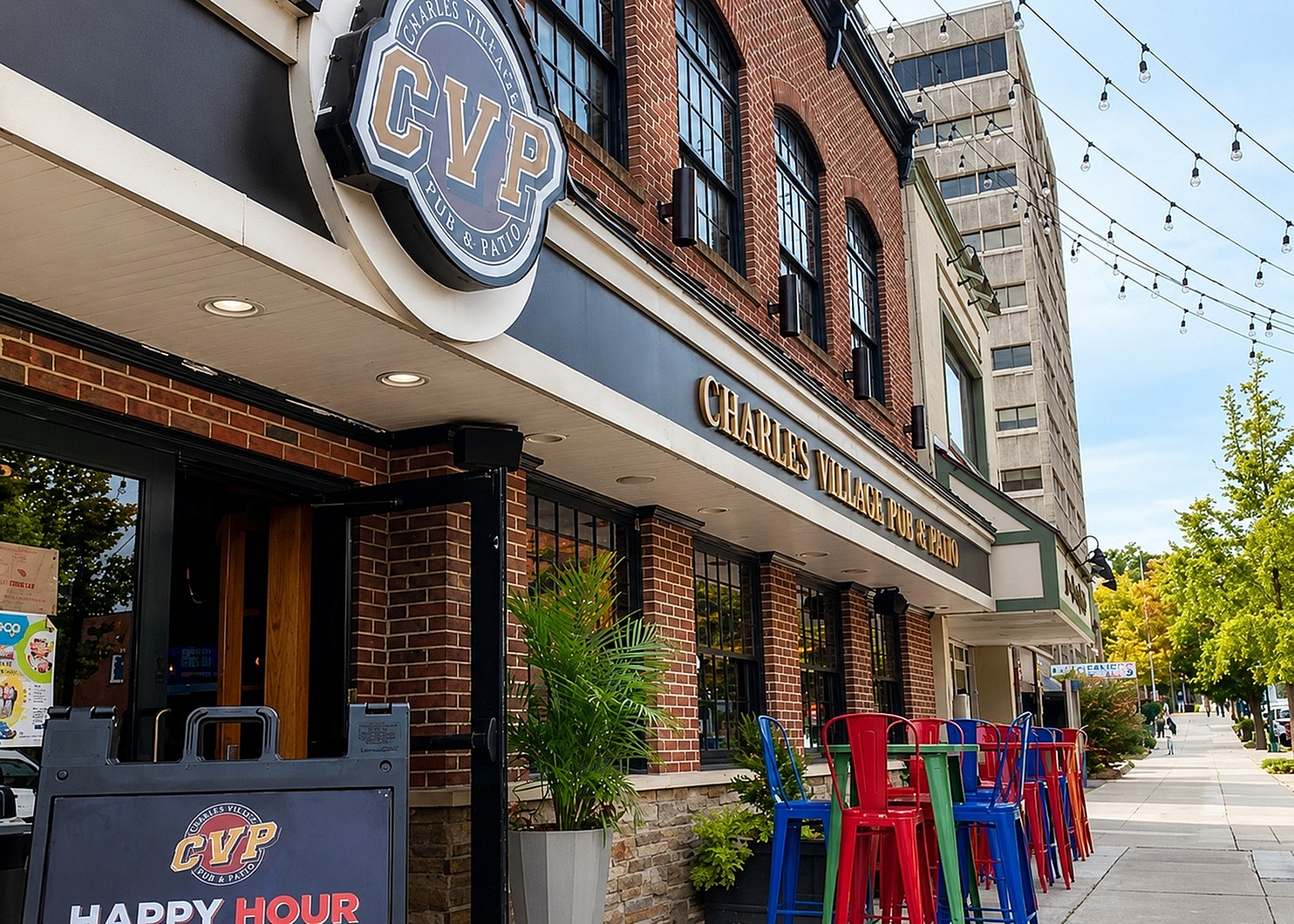 Vibrant street view of Charles Village Pub & Patio with colorful seating, inviting entrance, and charming brick facade beneath string lights.