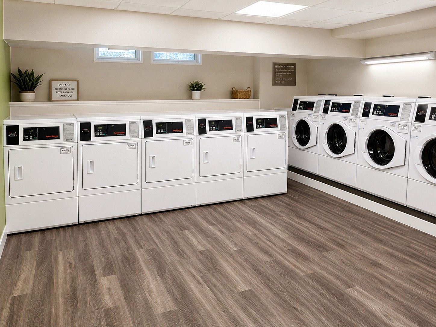 Modern apartment laundry room featuring multiple high-efficiency washers and dryers with sleek hardwood flooring and ambient lighting.