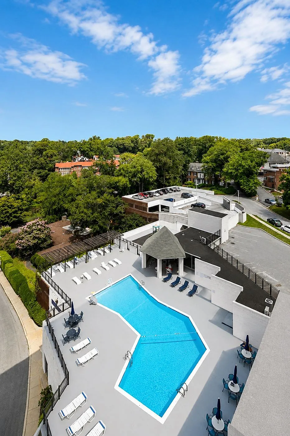 Inviting aerial view of a modern apartment complex featuring a pristine swimming pool, lounge chairs, and vibrant green surroundings.