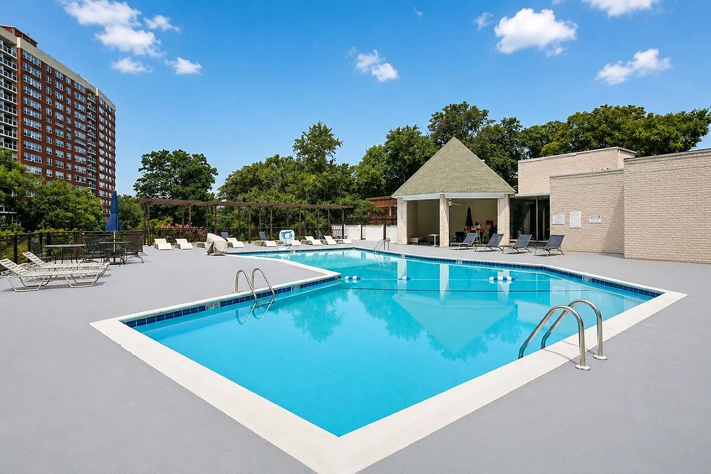 Inviting outdoor pool area with sparkling blue water, surrounded by lush greenery and modern lounge chairs, perfect for relaxation and leisure.