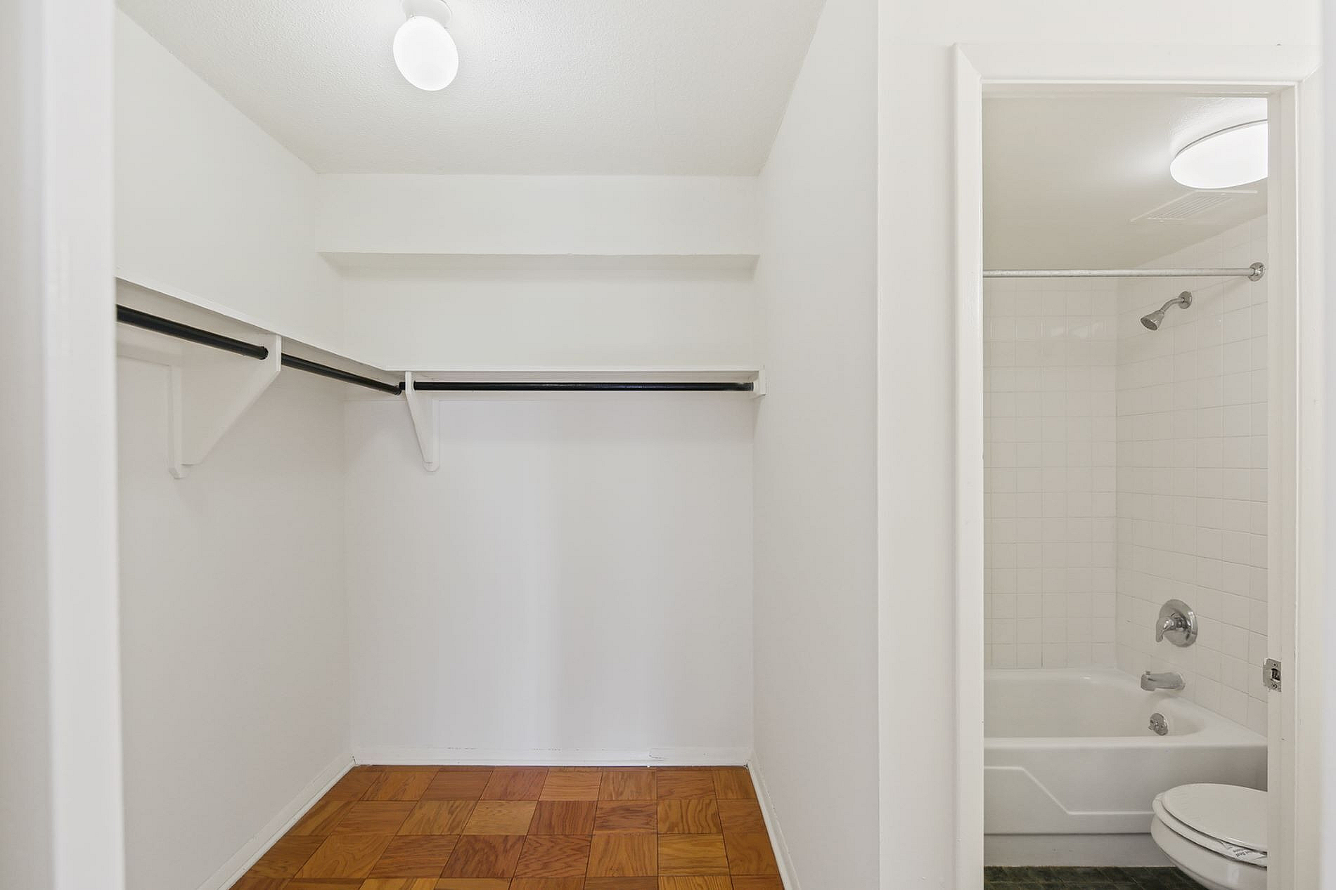 Spacious walk-in closet with hardwood flooring and adjacent bathroom featuring a sleek white bathtub and modern fixtures.
