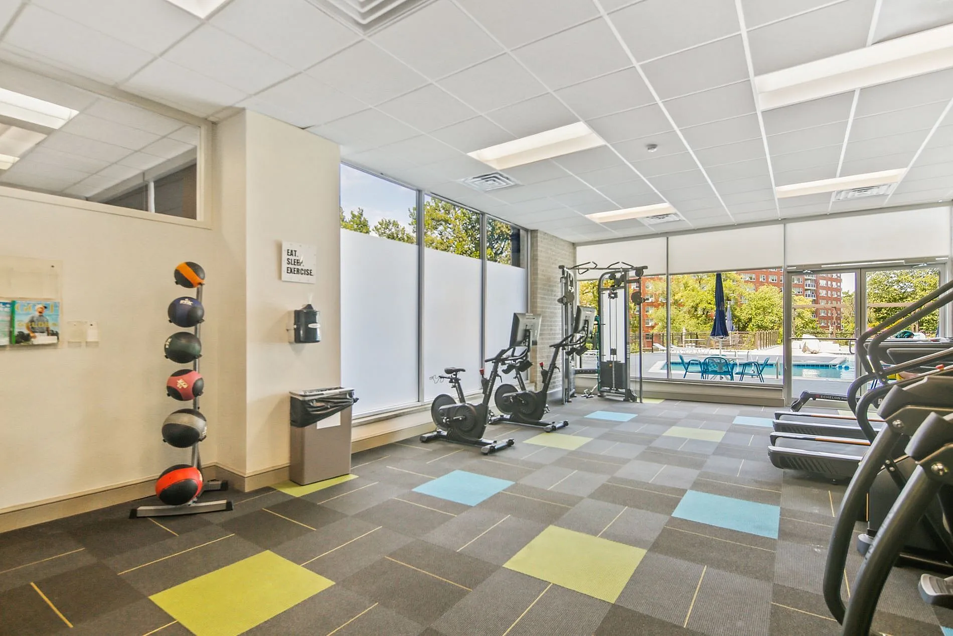 Modern fitness center with state-of-the-art equipment, vibrant flooring, and large windows overlooking a pool area.