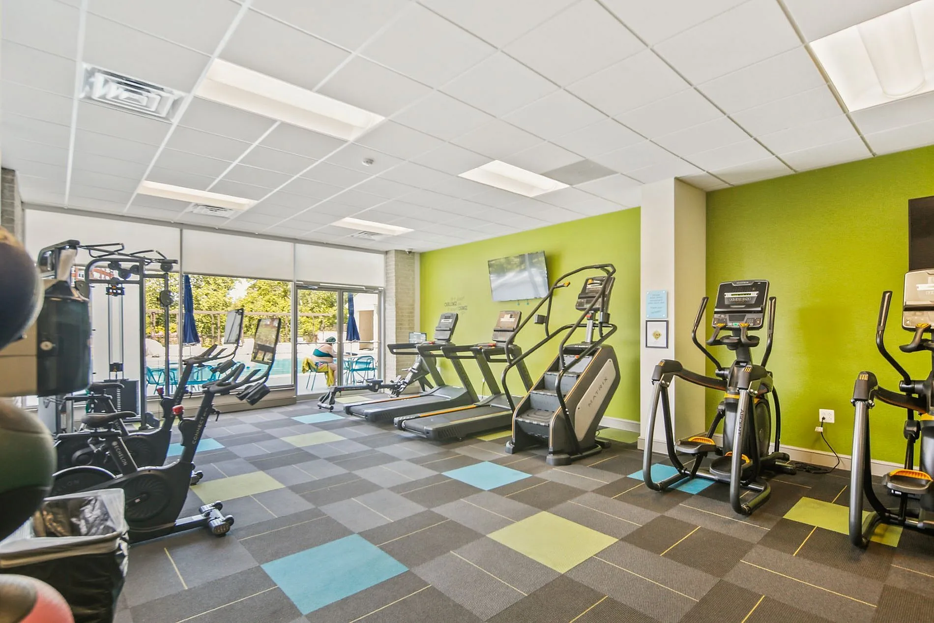 Bright and modern fitness center with state-of-the-art equipment, featuring treadmills and ellipticals, overlooking a sunlit outdoor pool area.