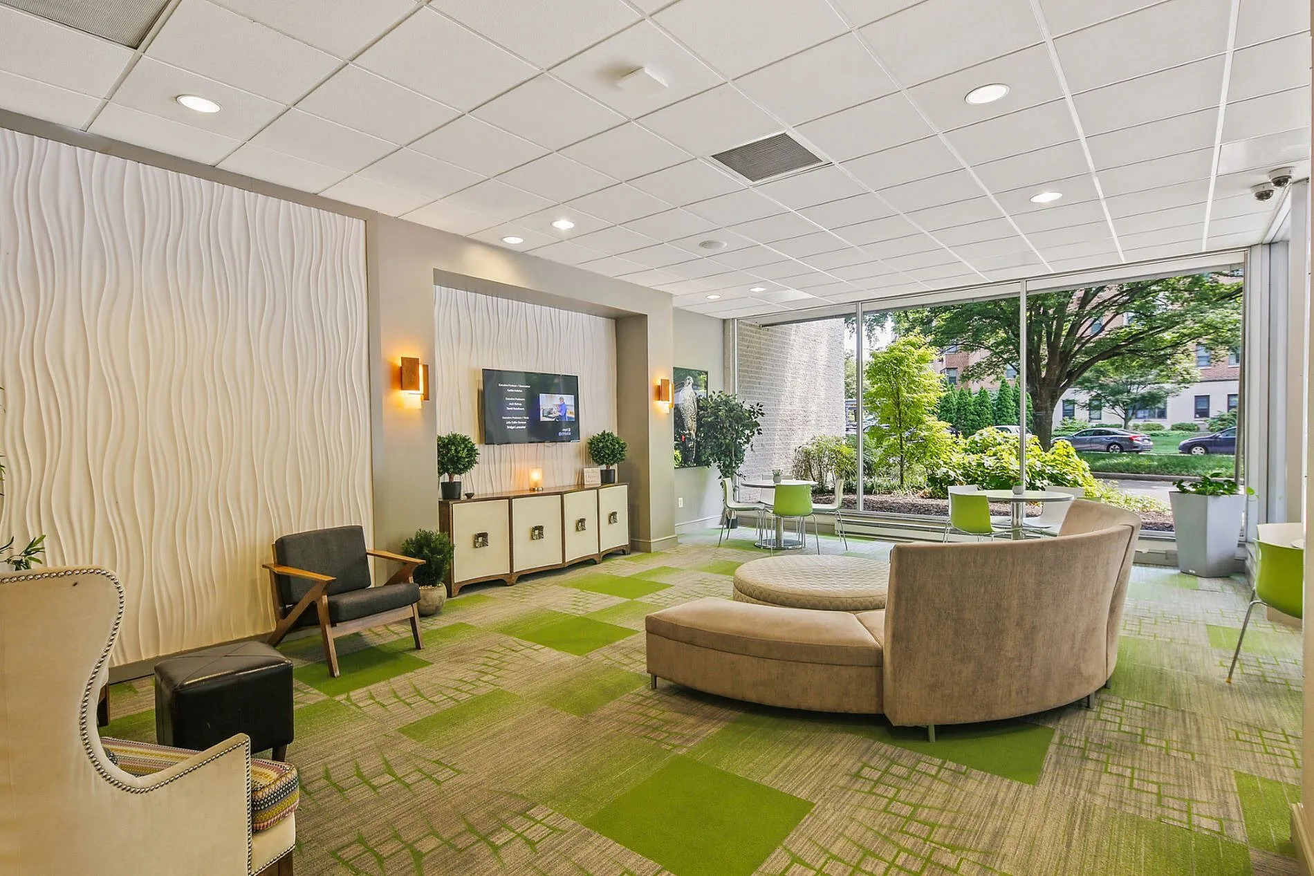 Contemporary lobby with stylish seating, vibrant green accents, and floor-to-ceiling windows showcasing lush outdoor views.