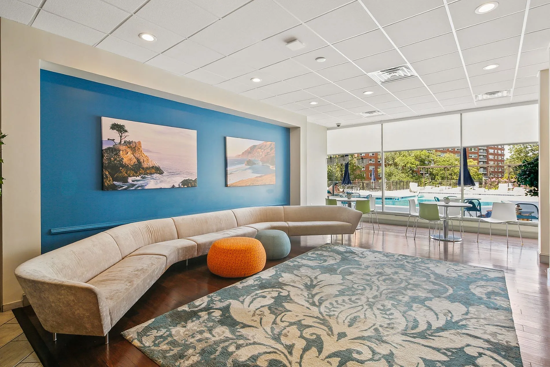 Inviting lounge area with modern curved sofa, vibrant artwork, and floor-to-ceiling windows overlooking a poolside view, creating a stylish and relaxing atmosphere.