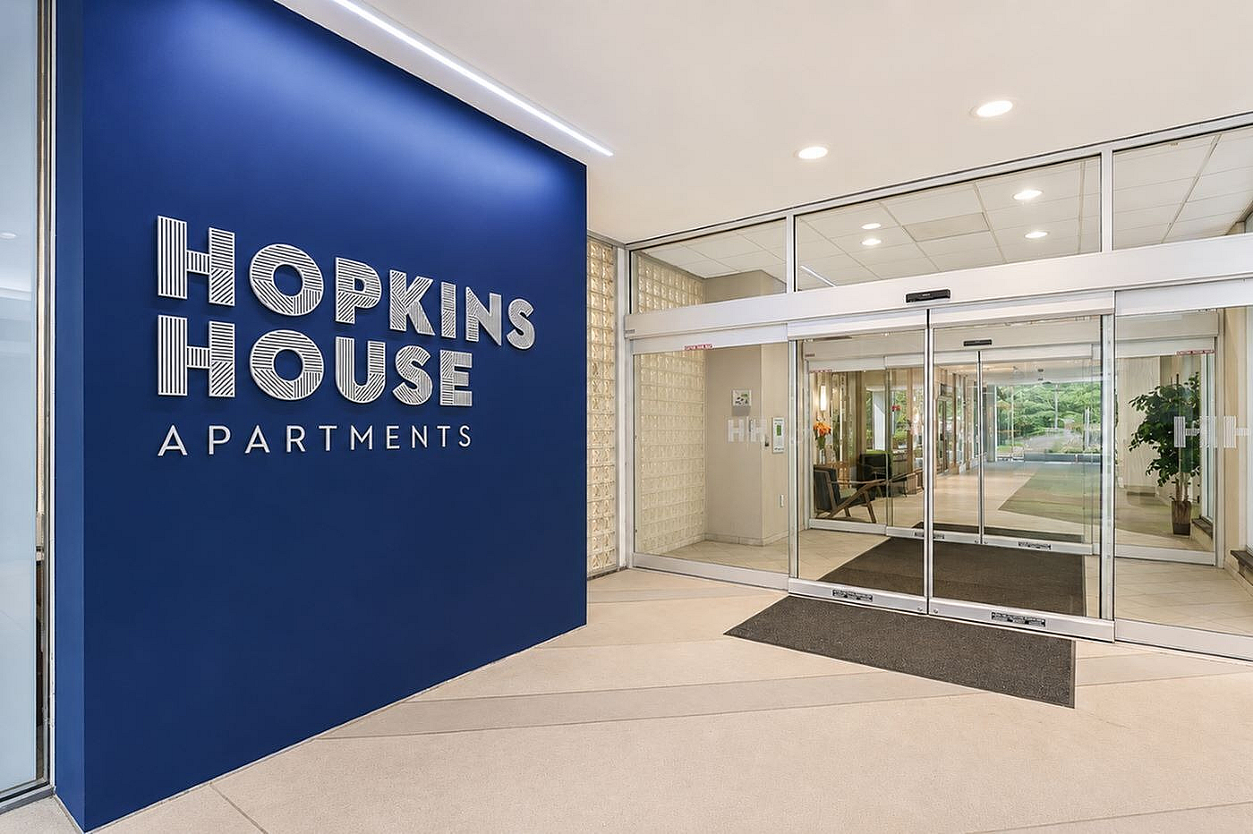 Inviting entrance of Hopkins House Apartments featuring elegant blue signage and modern glass doors.