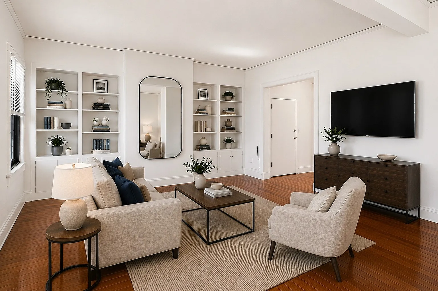 Bright and inviting living room with elegant furniture, hardwood floors, built-in shelves, and a stylish mirror.