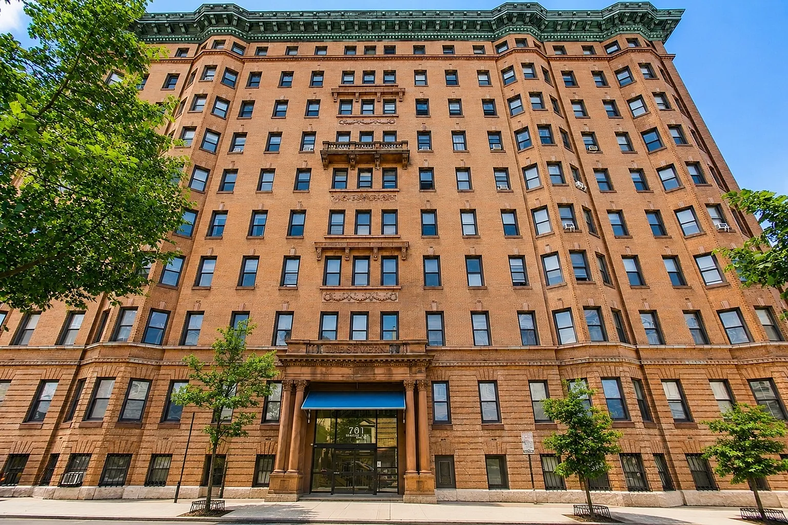 Majestic historic brick apartment building with charming architectural details, framed by lush green trees, promising elegant urban living.