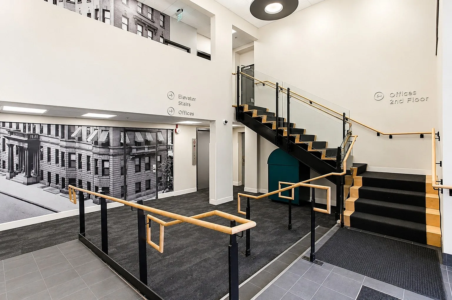Modern lobby with elegant staircase, featuring a black and white vintage mural, and sleek wood-accented railings for a contemporary feel.
