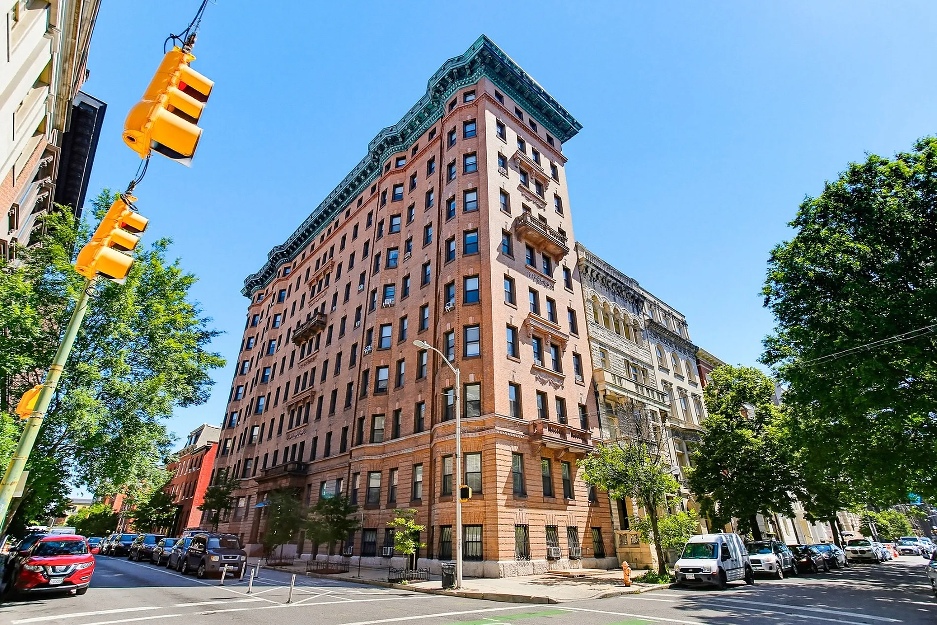 Charming corner building with classic architecture, nestled in a vibrant neighborhood with lush green trees and bright urban surroundings.
