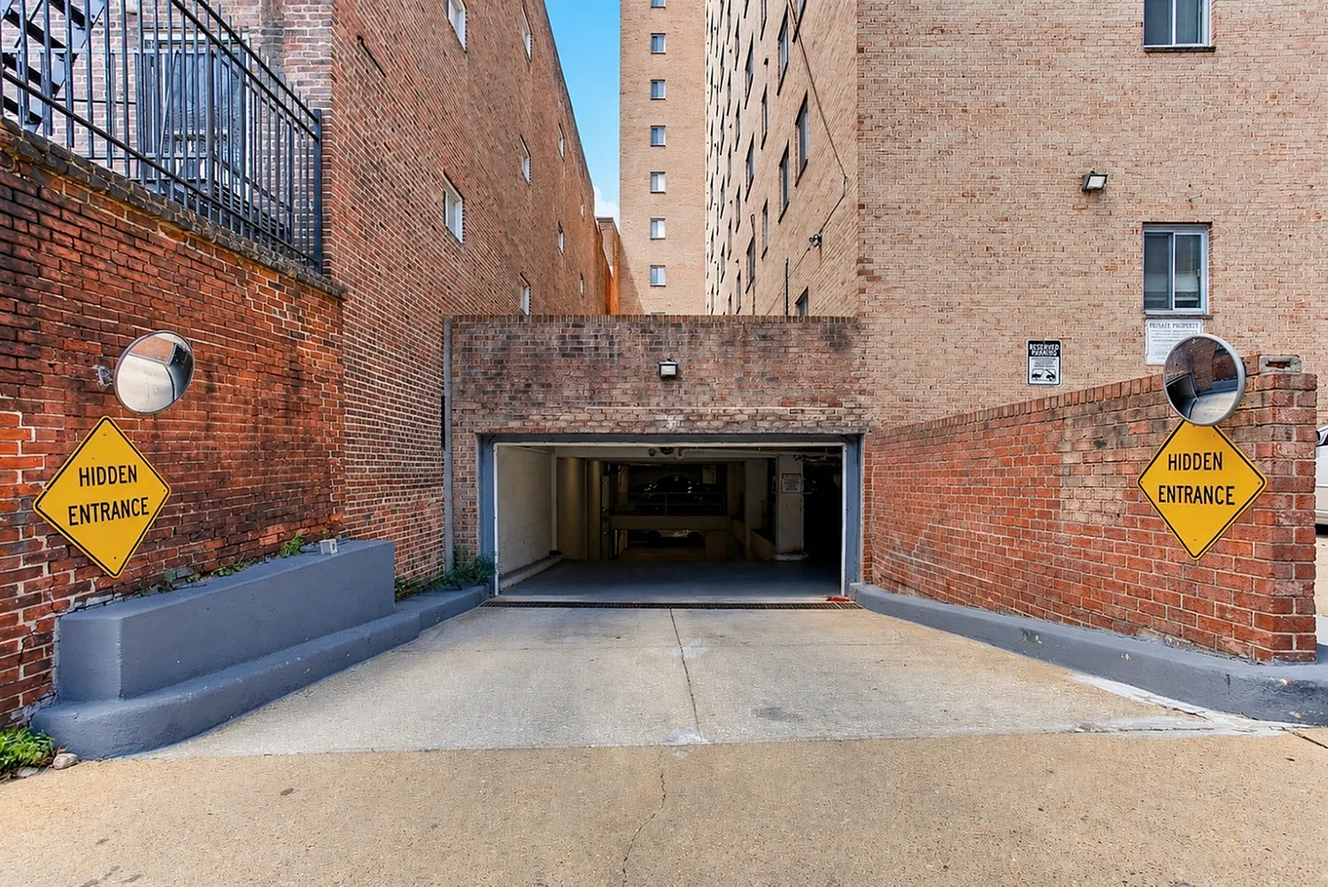 Charming brick-walled entrance to a secure underground parking area, highlighted by 'Hidden Entrance' signs for convenience and privacy.