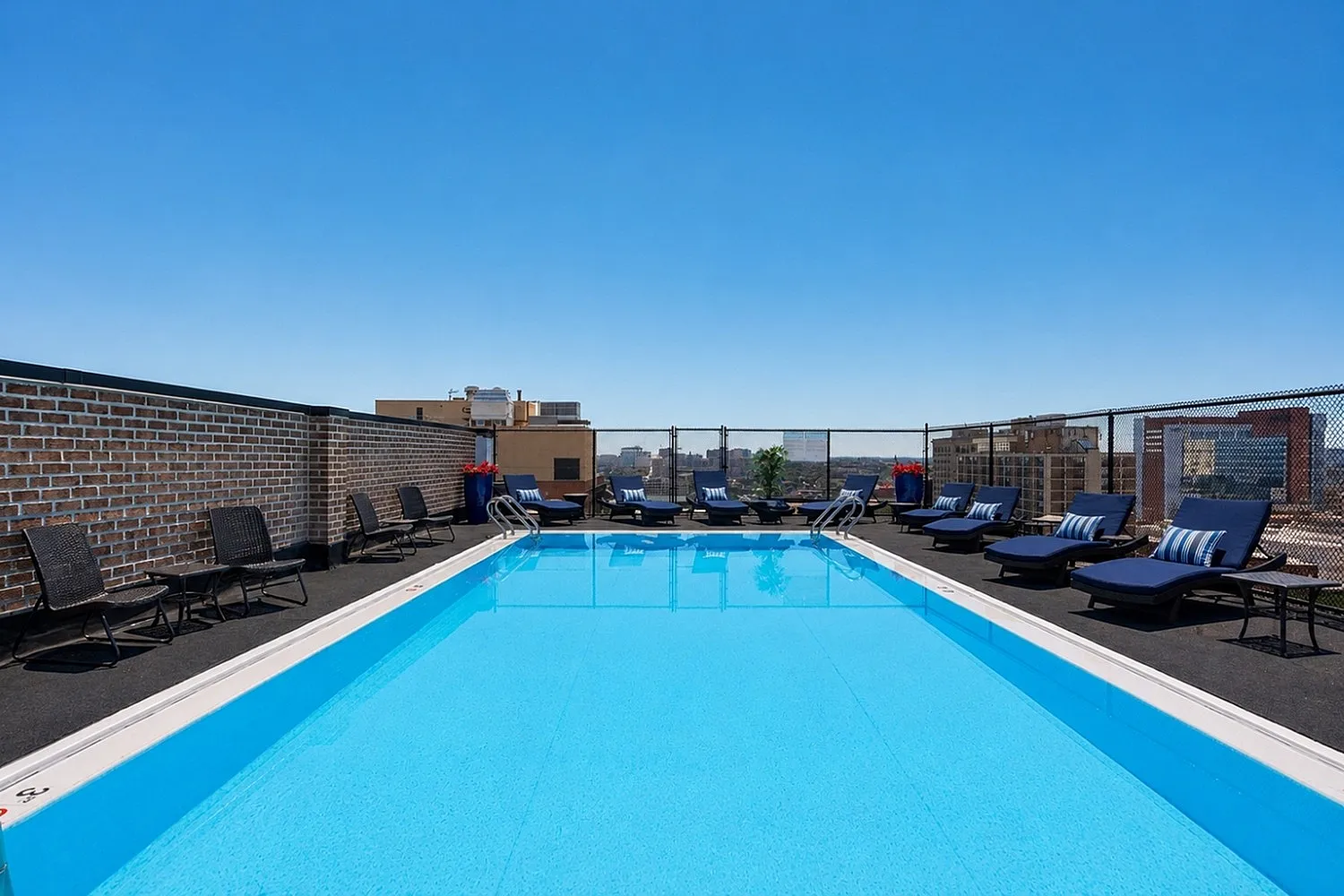 Luxurious rooftop pool with chic lounge chairs and stunning cityscape views on a clear day.
