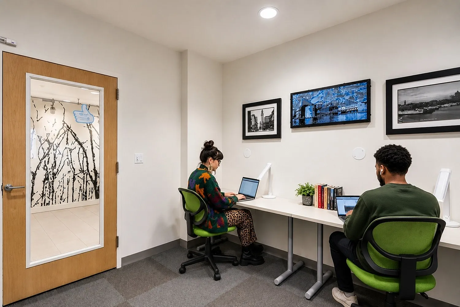 Modern co-working space featuring two people working at laptops on a sleek white desk with vibrant green chairs, contemporary art on the walls, and ample lighting.