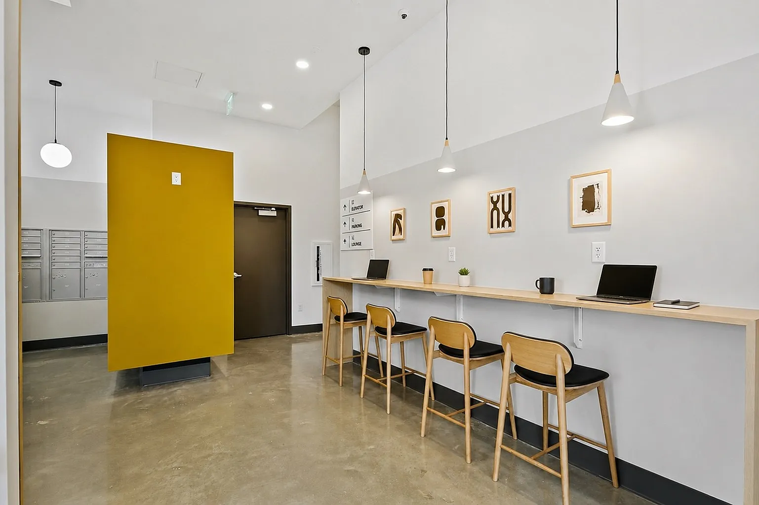 Modern communal workspace featuring a sleek long counter with stylish wooden stools, pendant lighting, and minimalist decor for a vibrant work environment.