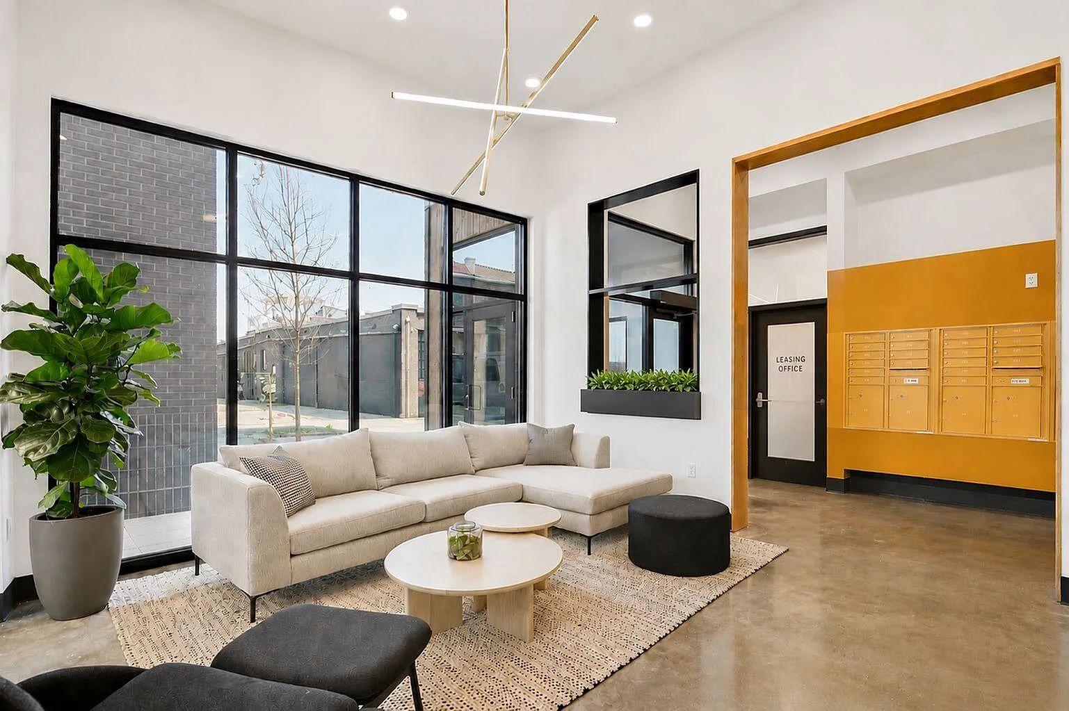Modern and inviting leasing office with a plush beige sectional, chic lighting fixture, and expansive windows offering natural light.
