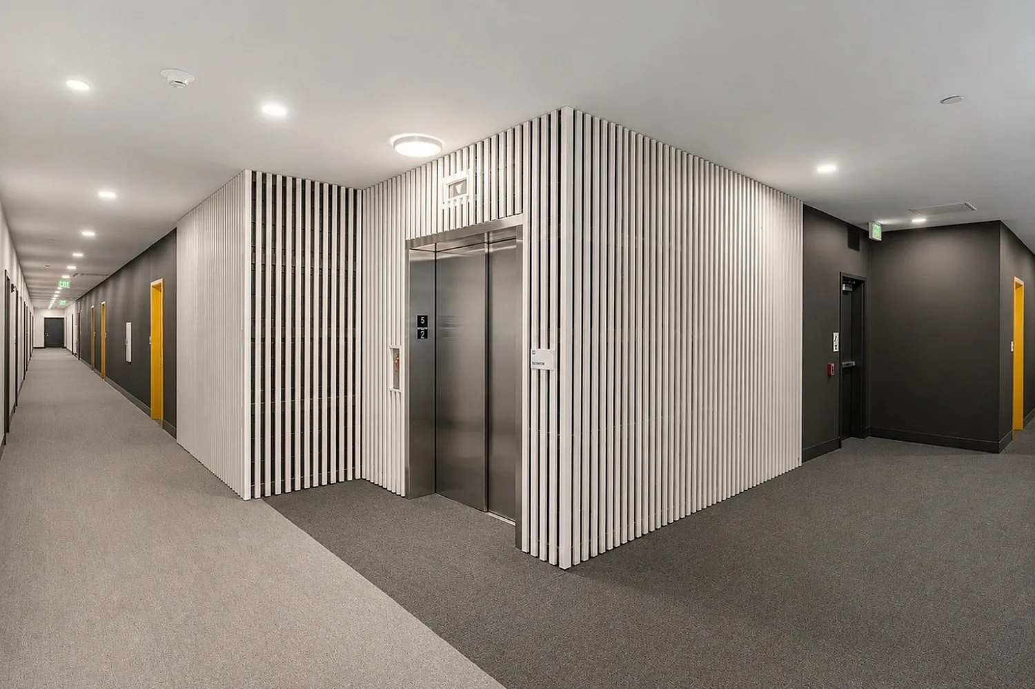 Modern apartment hallway with sleek design featuring stylish lighting, contemporary elevator, and vibrant yellow door accents.