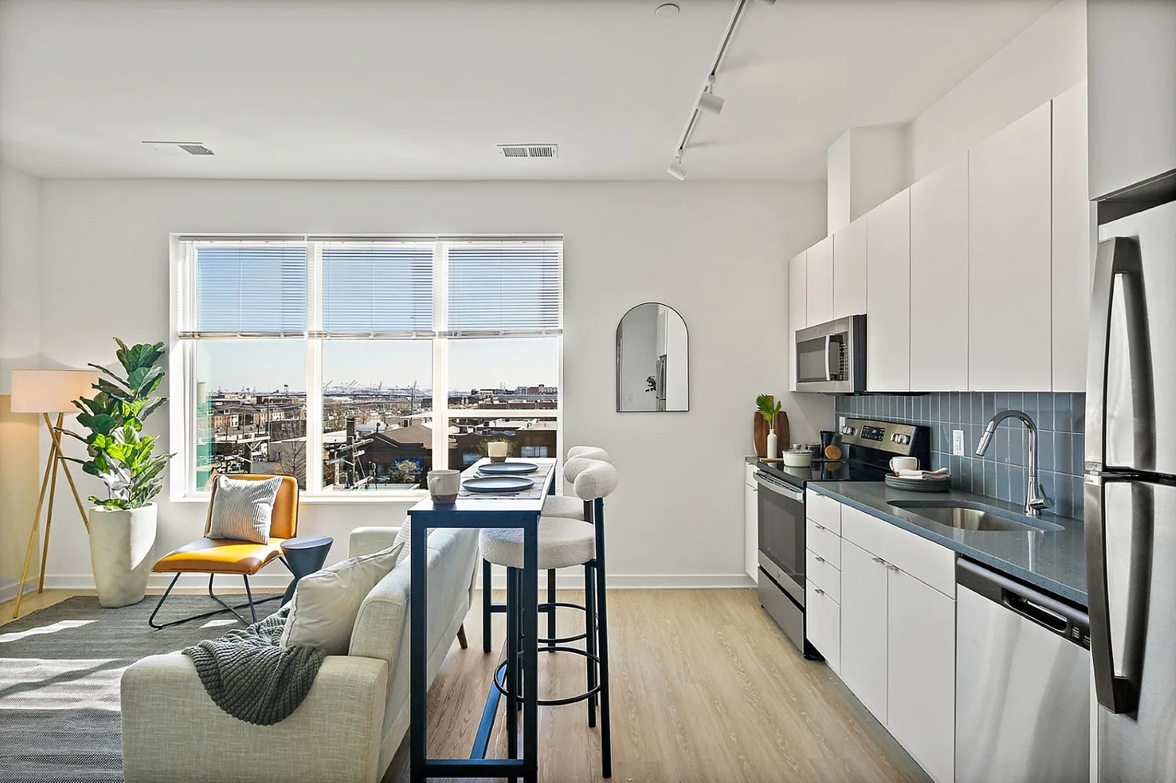 Bright and modern open-concept living space with sleek kitchen, stylish furniture, and cityscape view through large windows.