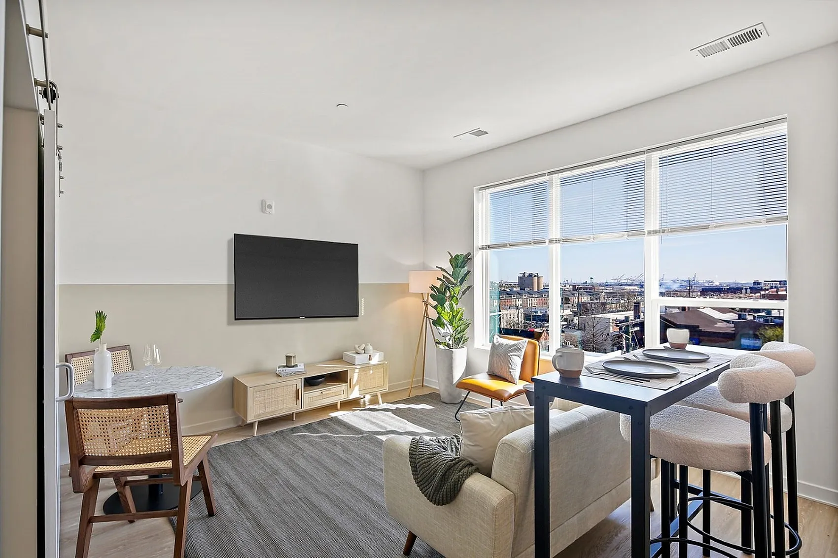Bright and modern living room with a large window offering cityscape views, stylish neutral decor, and comfortable seating.