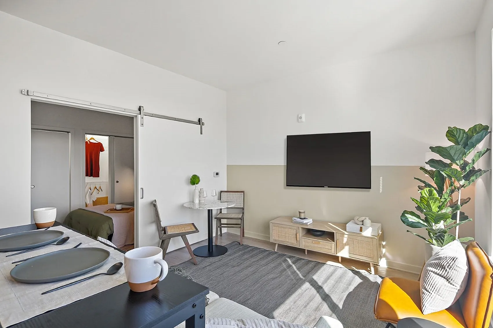 Bright modern living space featuring elegant dining setup, cozy seating area, flat-screen TV, and stylish bedroom entry.