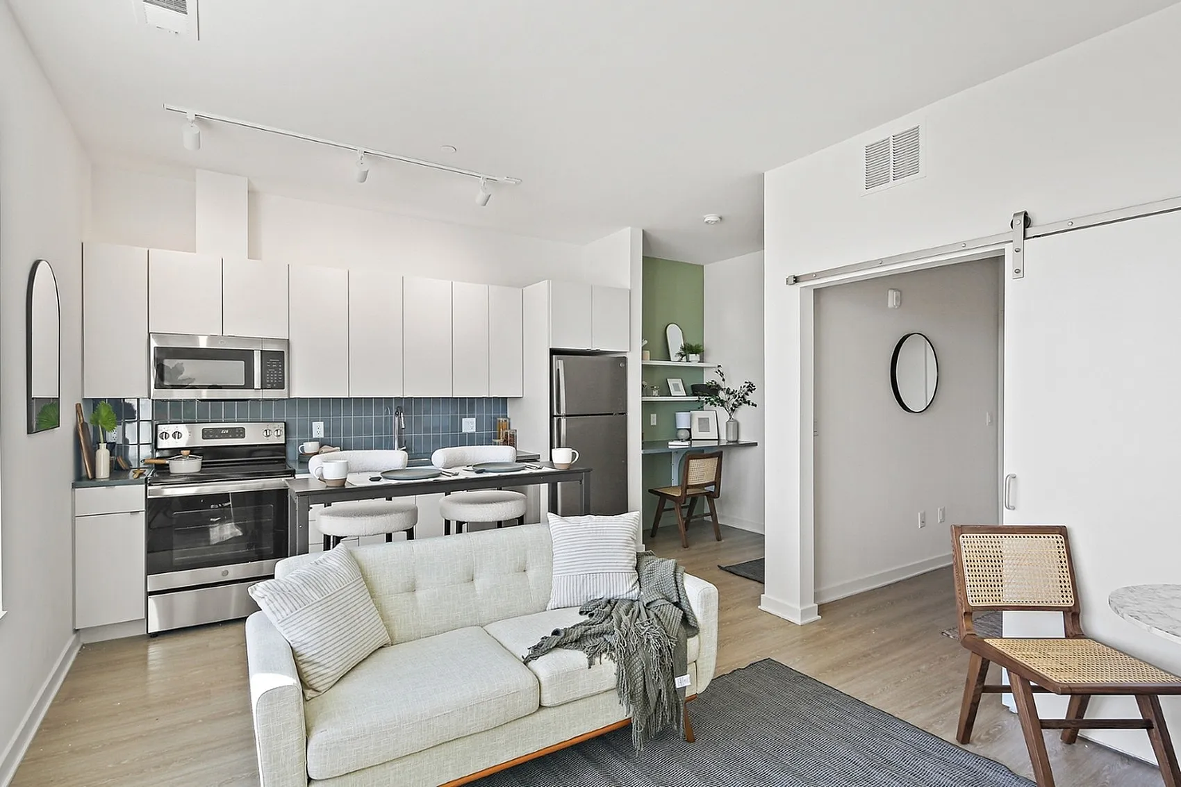 Modern open-plan living space featuring a sleek kitchen with stainless steel appliances and chic white cabinetry, cozy living area with a stylish sofa, and a functional workspace.