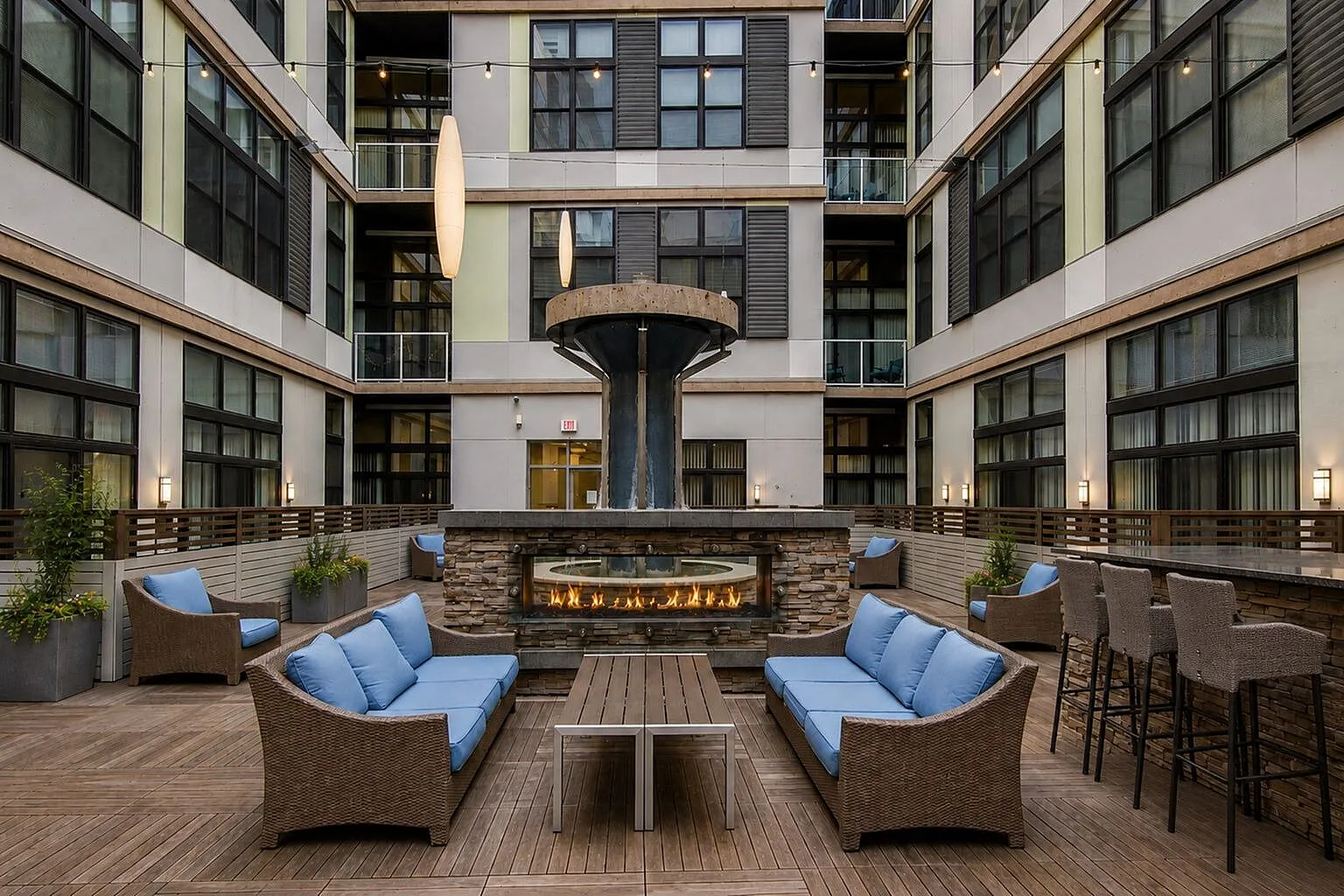 Luxurious apartment courtyard with elegant seating, modern fire pit, and ambient string lighting creating an inviting atmosphere.