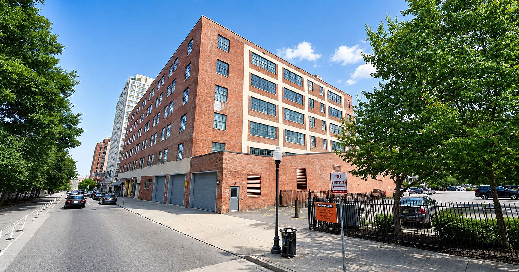 Charming urban apartment building with a classic red brick exterior, nestled in a lively city street lined with lush green trees.