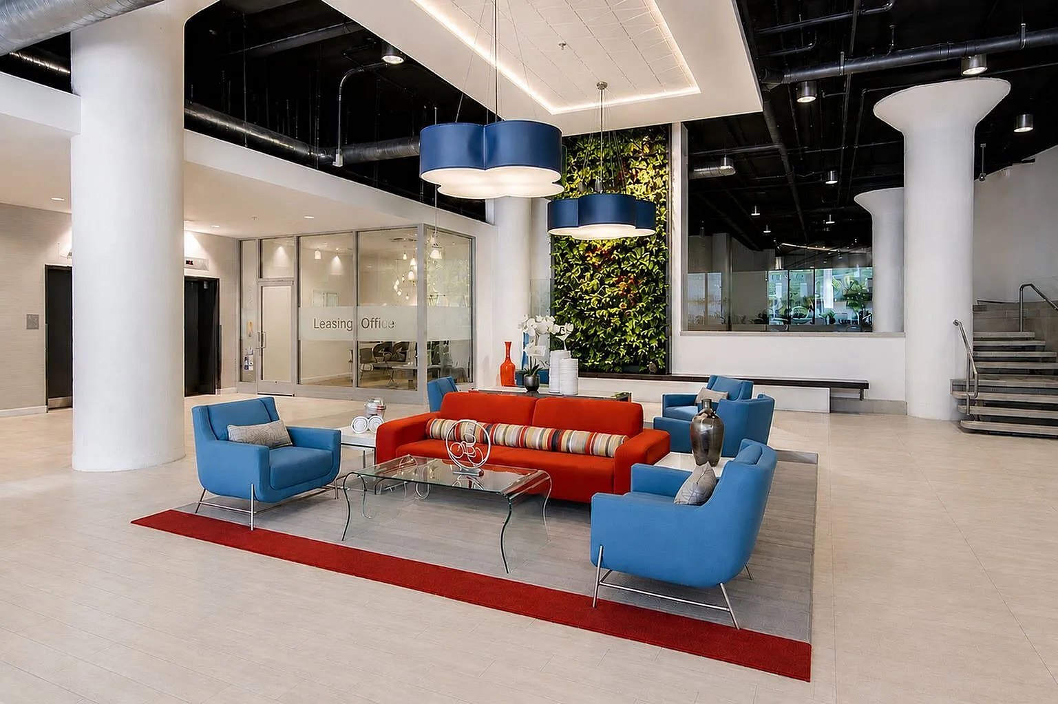 Modern apartment lobby featuring vibrant blue and red seating, elegant glass coffee table, striking vertical garden, and stylish lighting fixtures.