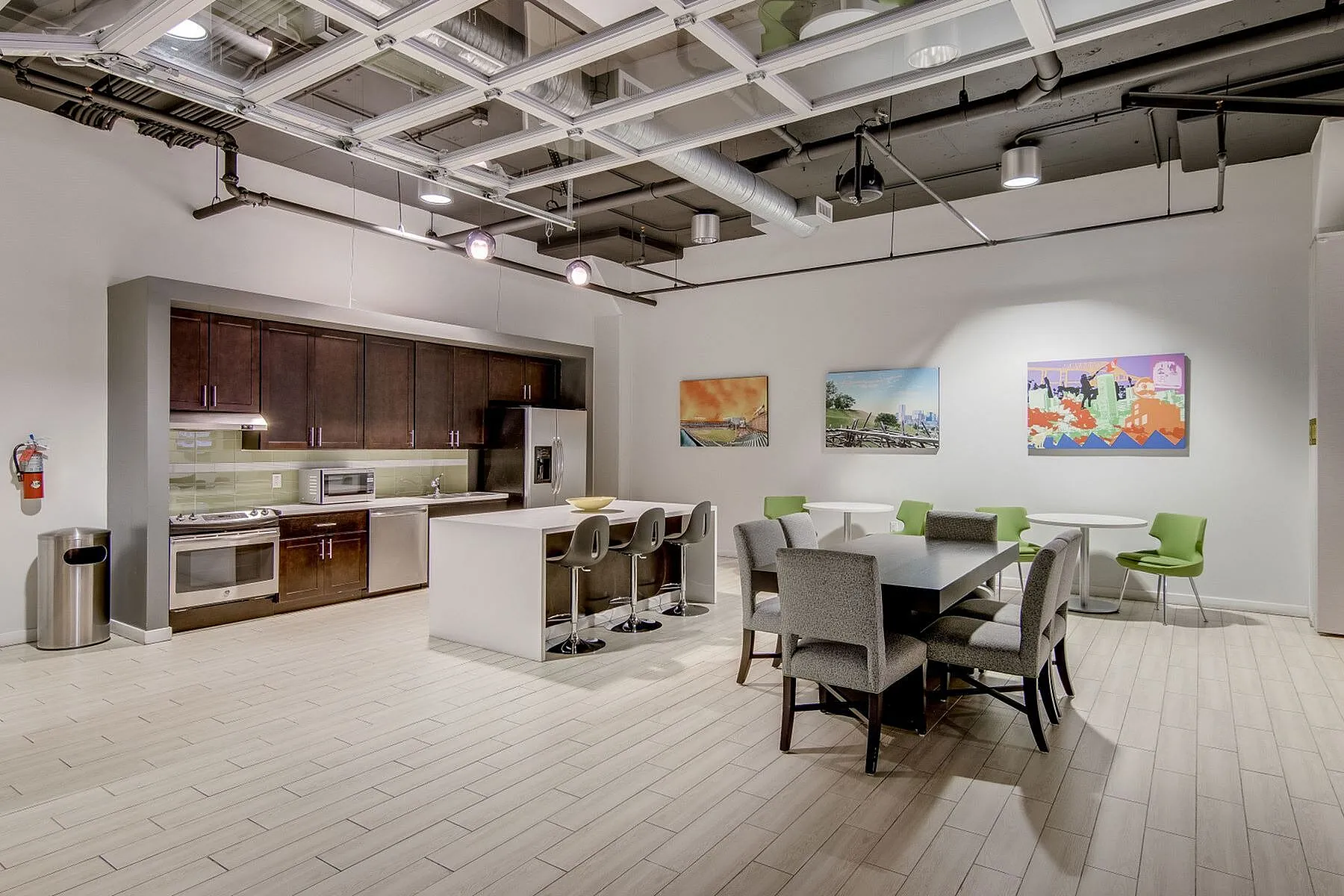 Contemporary kitchen and dining area featuring sleek cabinetry, modern appliances, elegant island with bar seating, and stylish artwork under industrial-style ceilings.