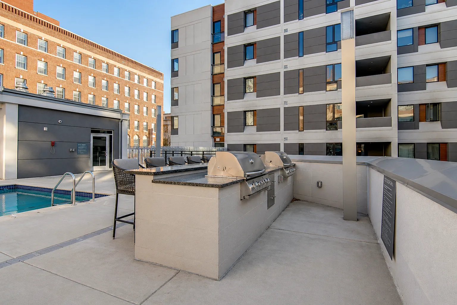 Contemporary apartment complex showcasing a stylish outdoor area with a sleek pool and modern barbecue stations, perfect for relaxation and entertainment.