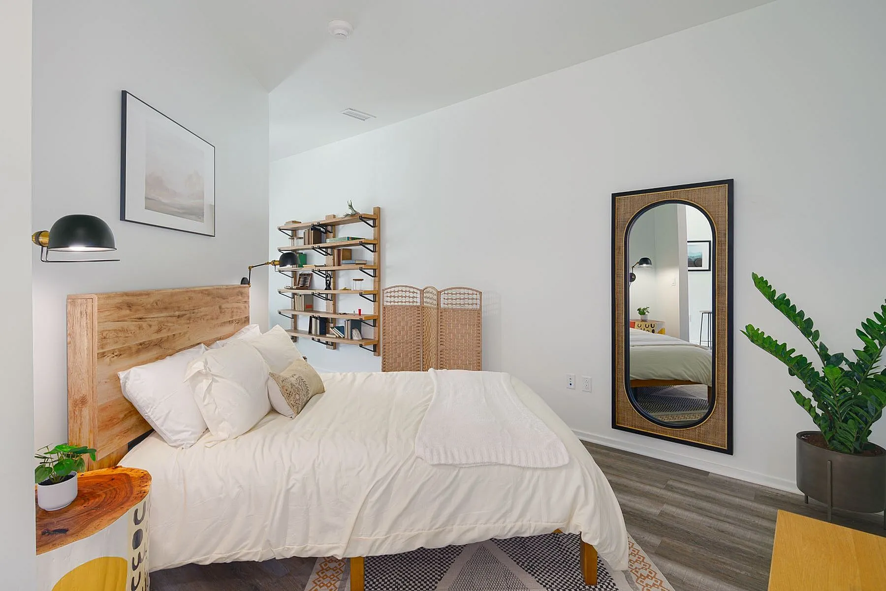 Tranquil bedroom with cozy decor, featuring a wooden bed frame, elegant shelving, and a stylish full-length mirror. Perfect blend of comfort and modern design.