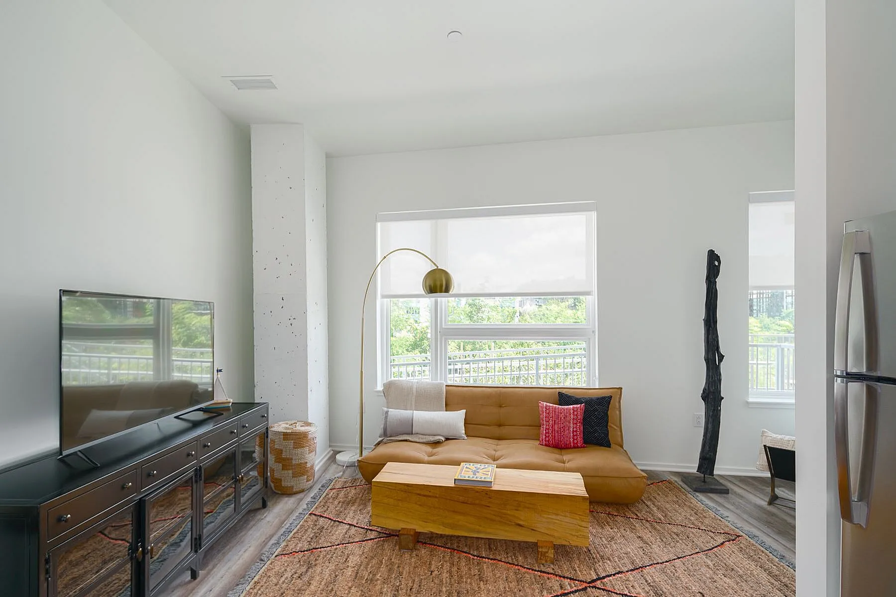 Bright, modern living room featuring a stylish tan sofa, large windows with a scenic view, and contemporary decor elements.