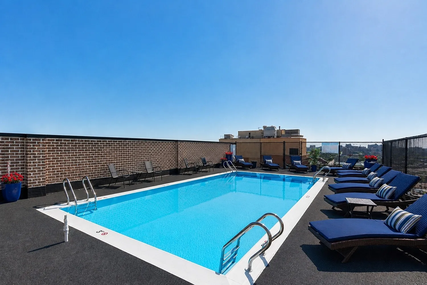 Luxurious rooftop swimming pool with chic lounge chairs and stunning city views under clear blue skies.